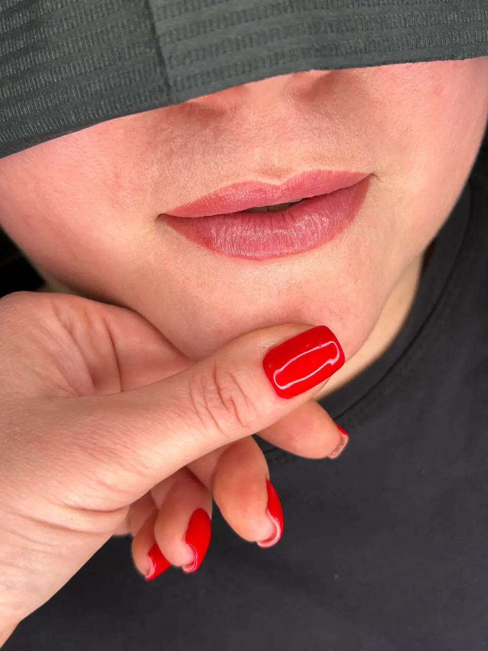 Close-up of a person with red nail polish touching their face against a black background hanafy soft beige lip pigment